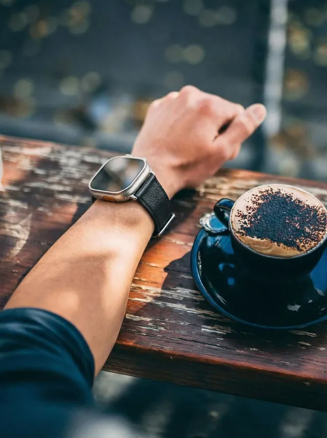 木のテーブルの上、MODIGIの黒い本革バンドを着けたApple Watchとコーヒー